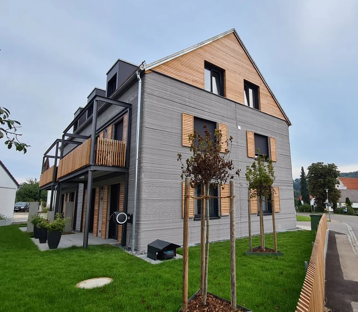 Corner view of grey 3d printed double storey concrete house with wooden cladding and garden