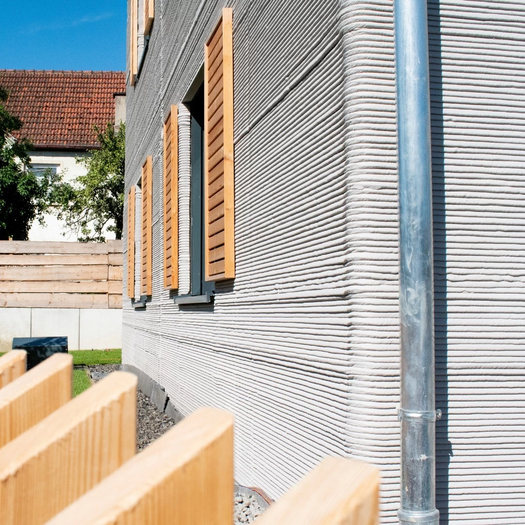 Corner view of grey 3d printed double storey concrete house with wooden shutters