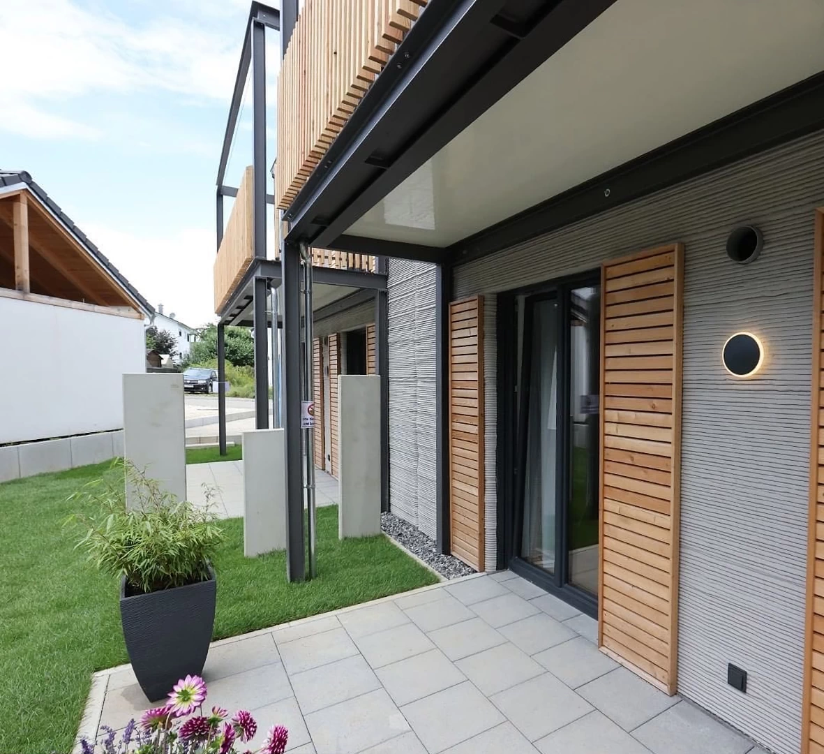 Front patio view of grey 3d printed double storey concrete house with wooden cladding and garden