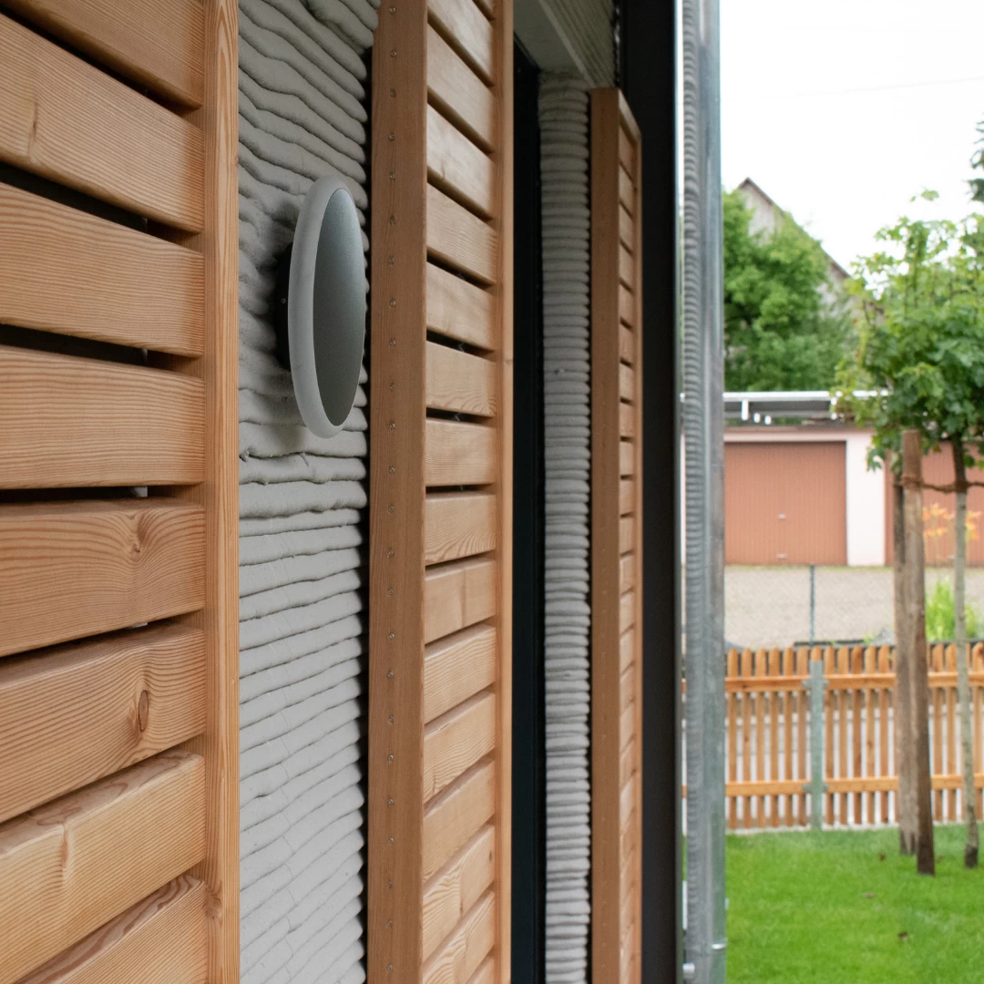 Side view of grey 3d printed concrete house with wooden shutters and garden