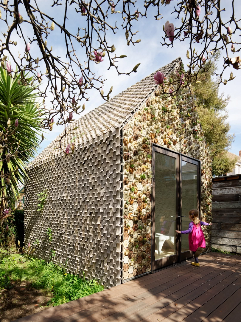 Corner view of colourful 3d printed ceramic cottage with wooden deck in a garden