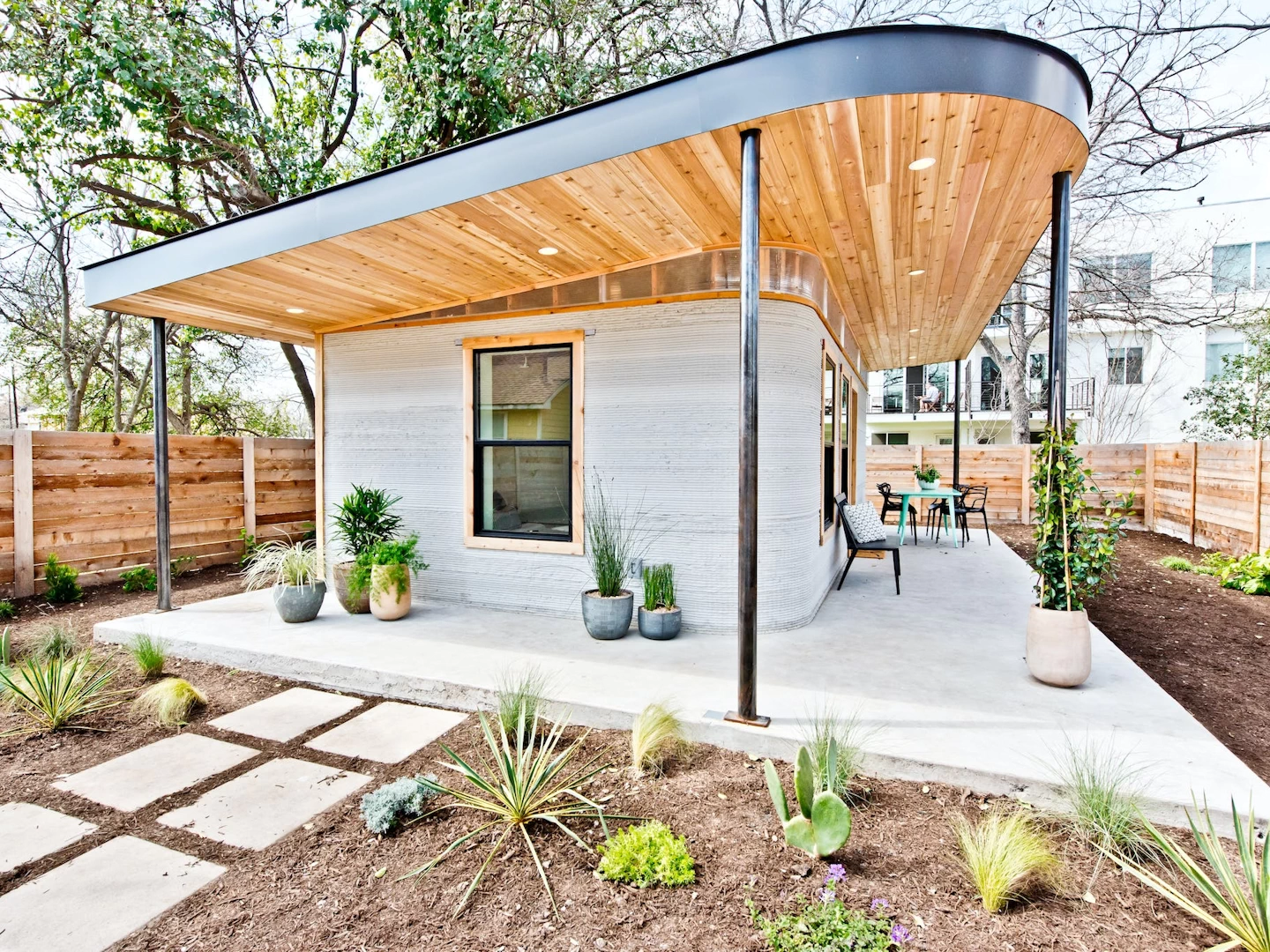 Corner view of grey 3d printed concrete house with wooden ceiling, garden and patio