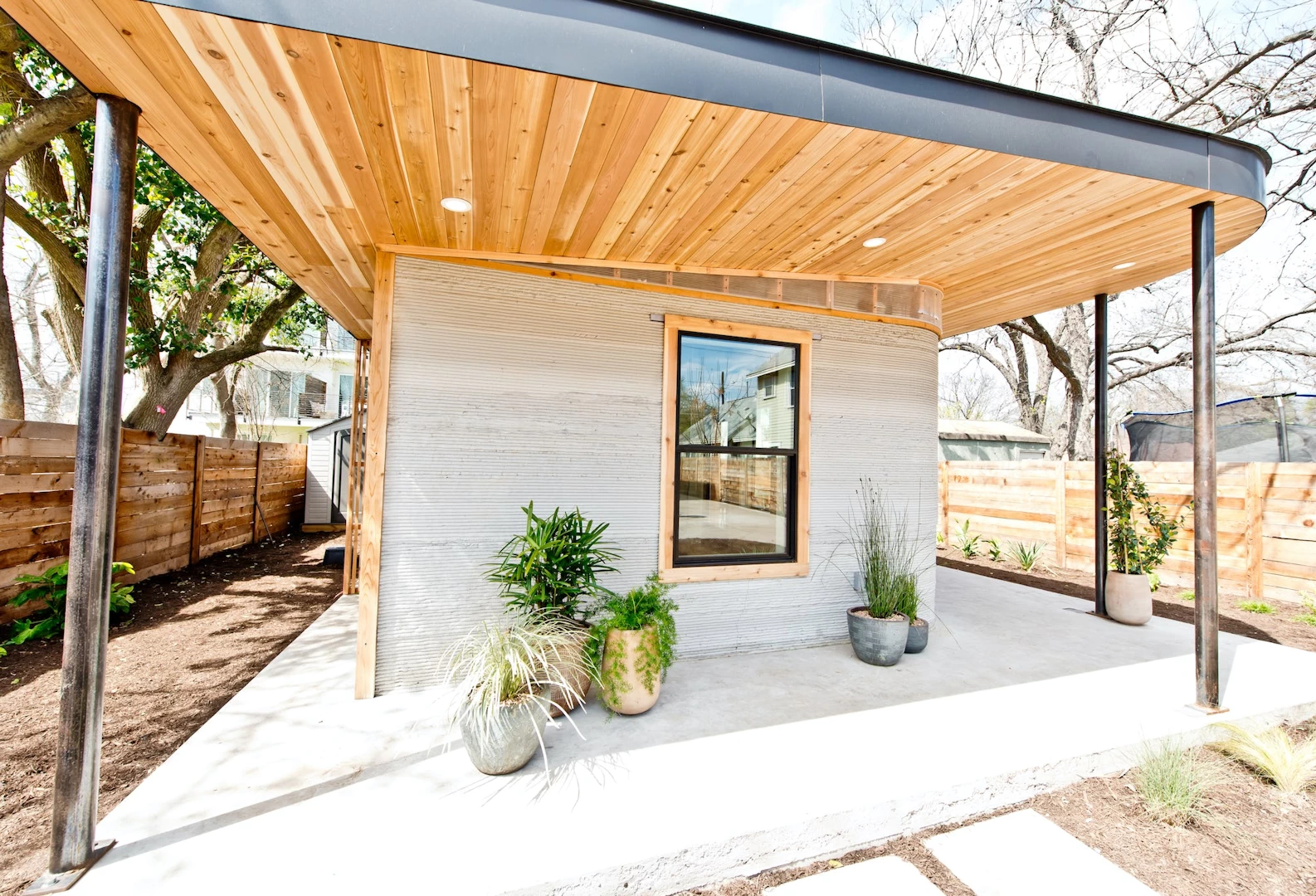 Side view of grey 3d printed concrete house with wooden ceiling, garden and patio