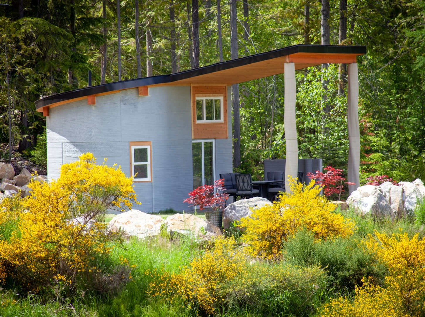 Side view of grey 3d printed double storey concrete house next to forest