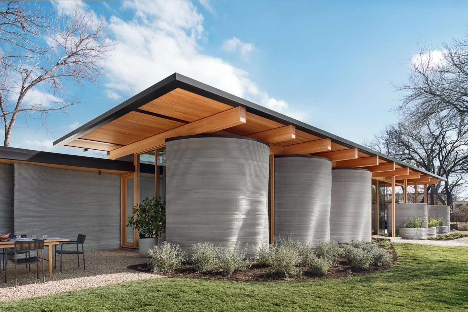 Corner view of curved grey 3d printed concrete house with wooden ceiling and garden