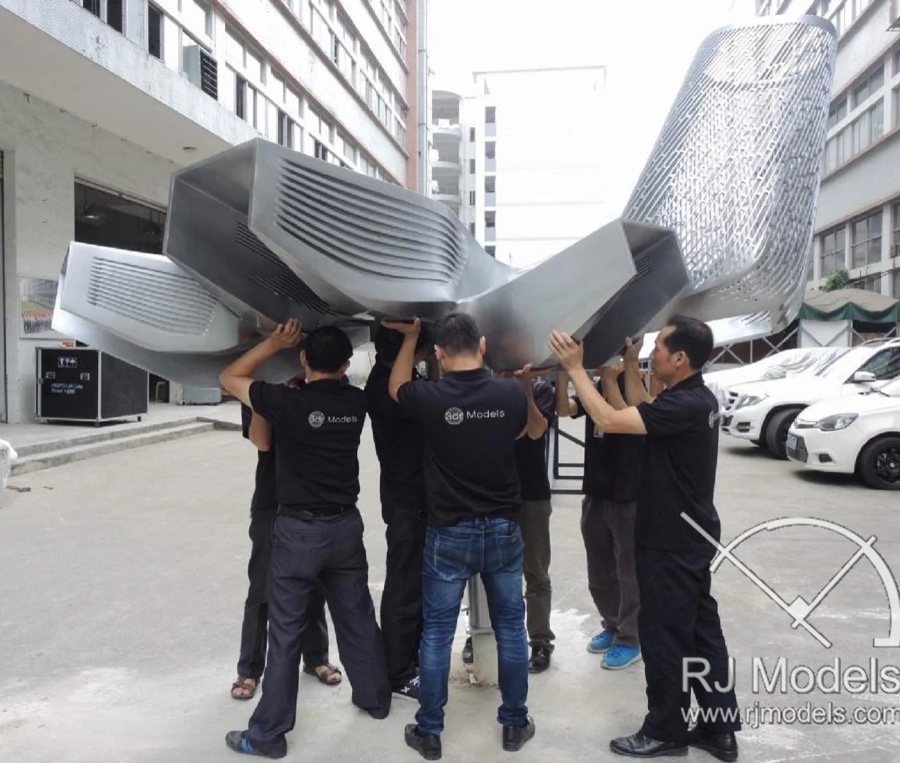 View of a model of a silver building shaped from curved rectangles and patterned shell 3d printed in plastic fdm being carried during assembly