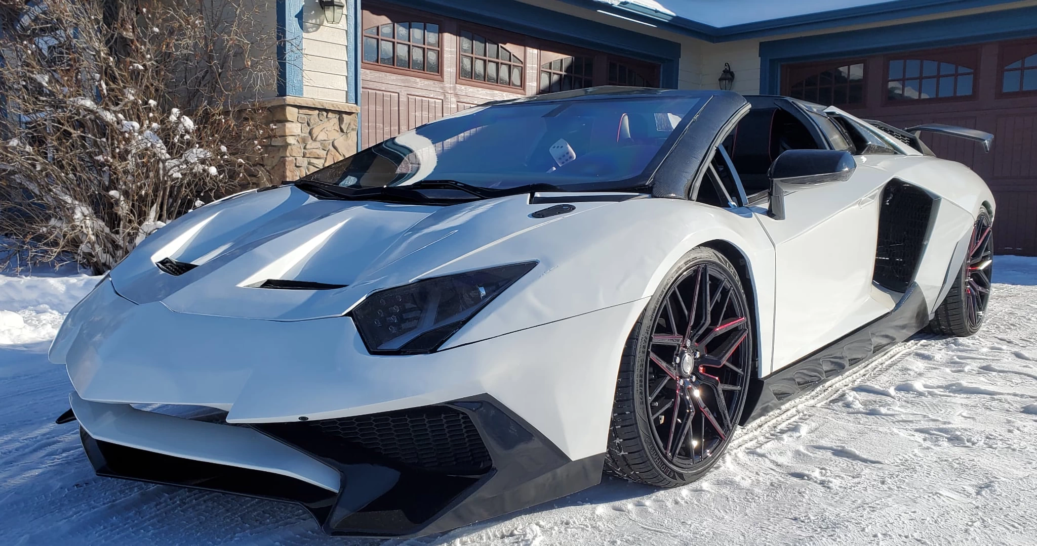 Front left view of a white 3d printed plastic lamborghini aventador on a driveway covered in snow