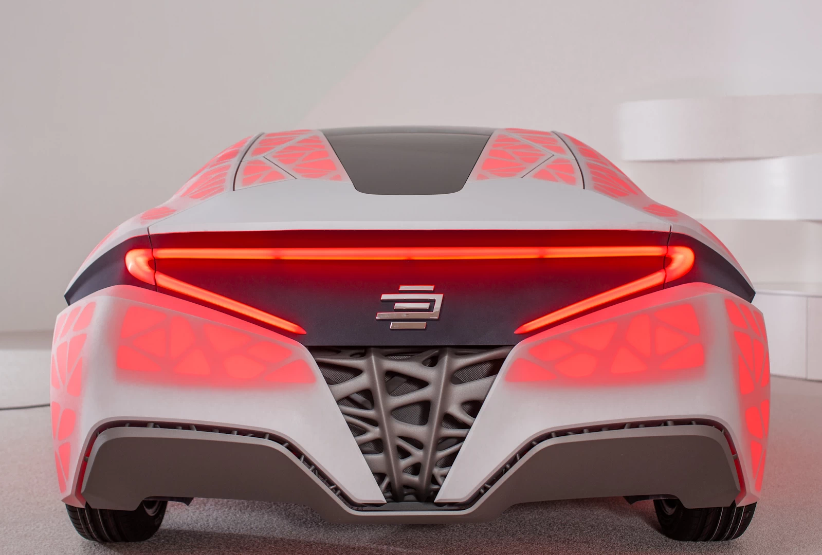 Rear view of a red and black supercar with a 3d printed resin mosaic body inside a white building