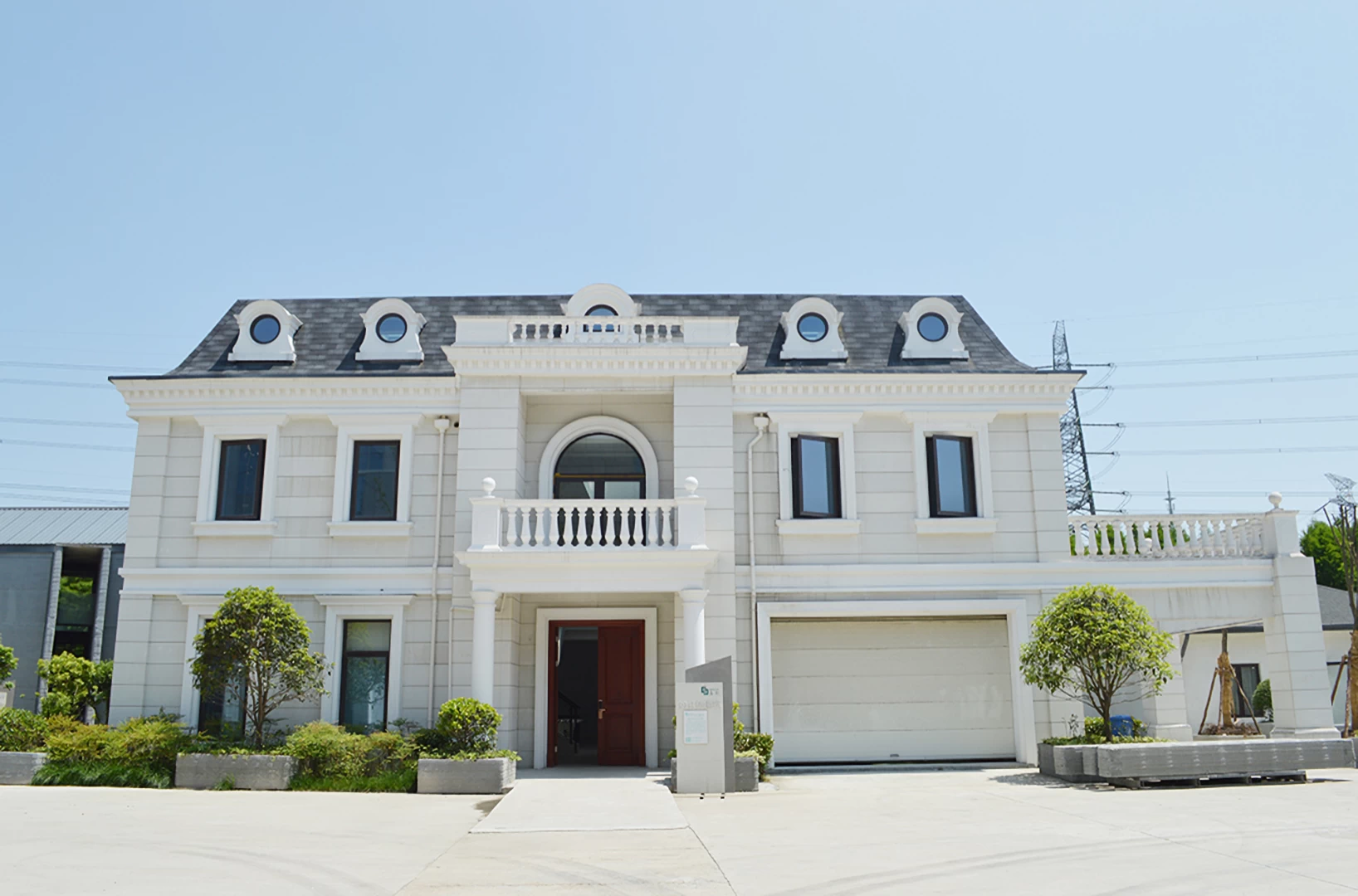 Front view of white 3d printed double storey concrete house with grey roof and surrounded by plants