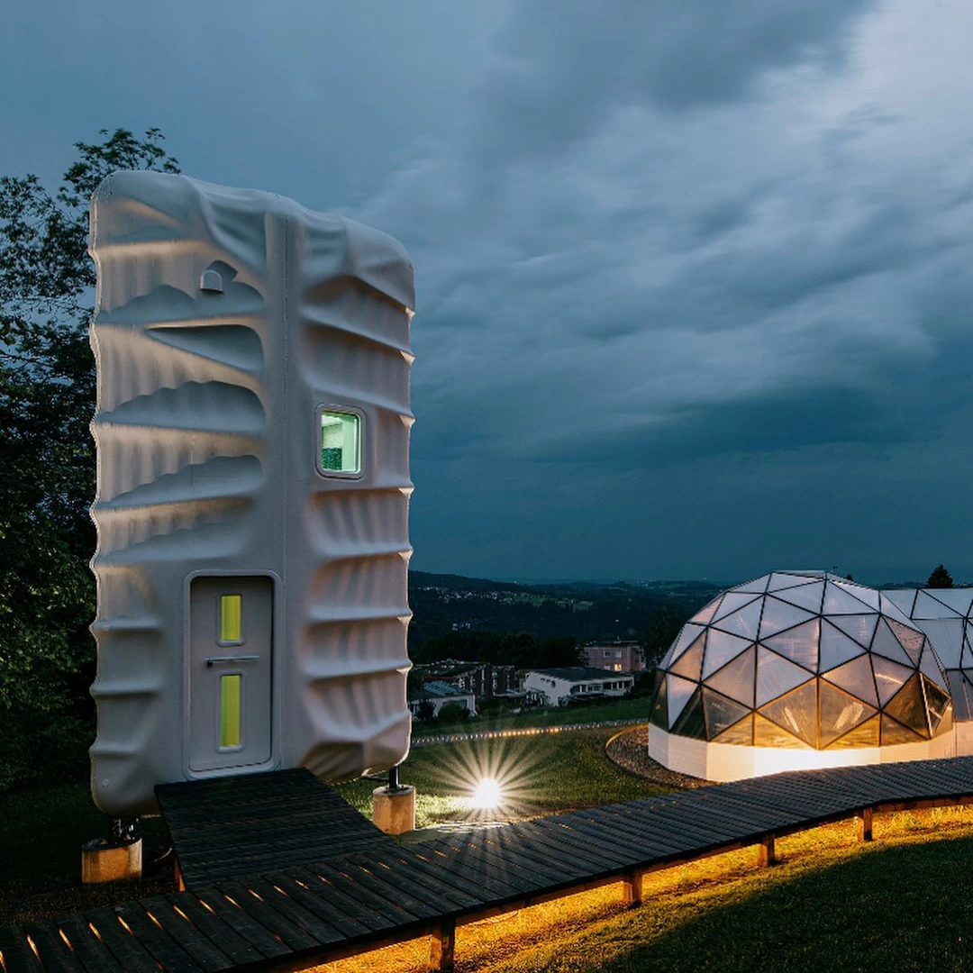 Front view of white 3d printed plastic habitat with wooden walkway next to geodesic dome