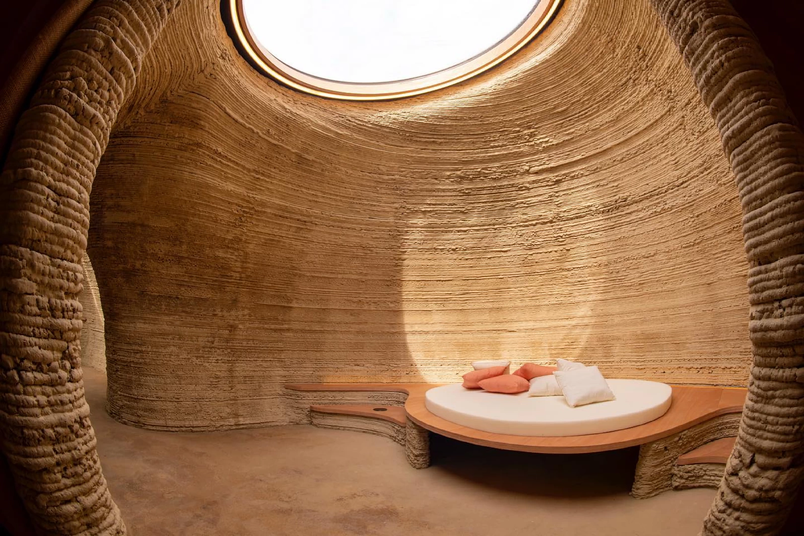 View of living area inside 3d printed clay house with curved walls and round sky light