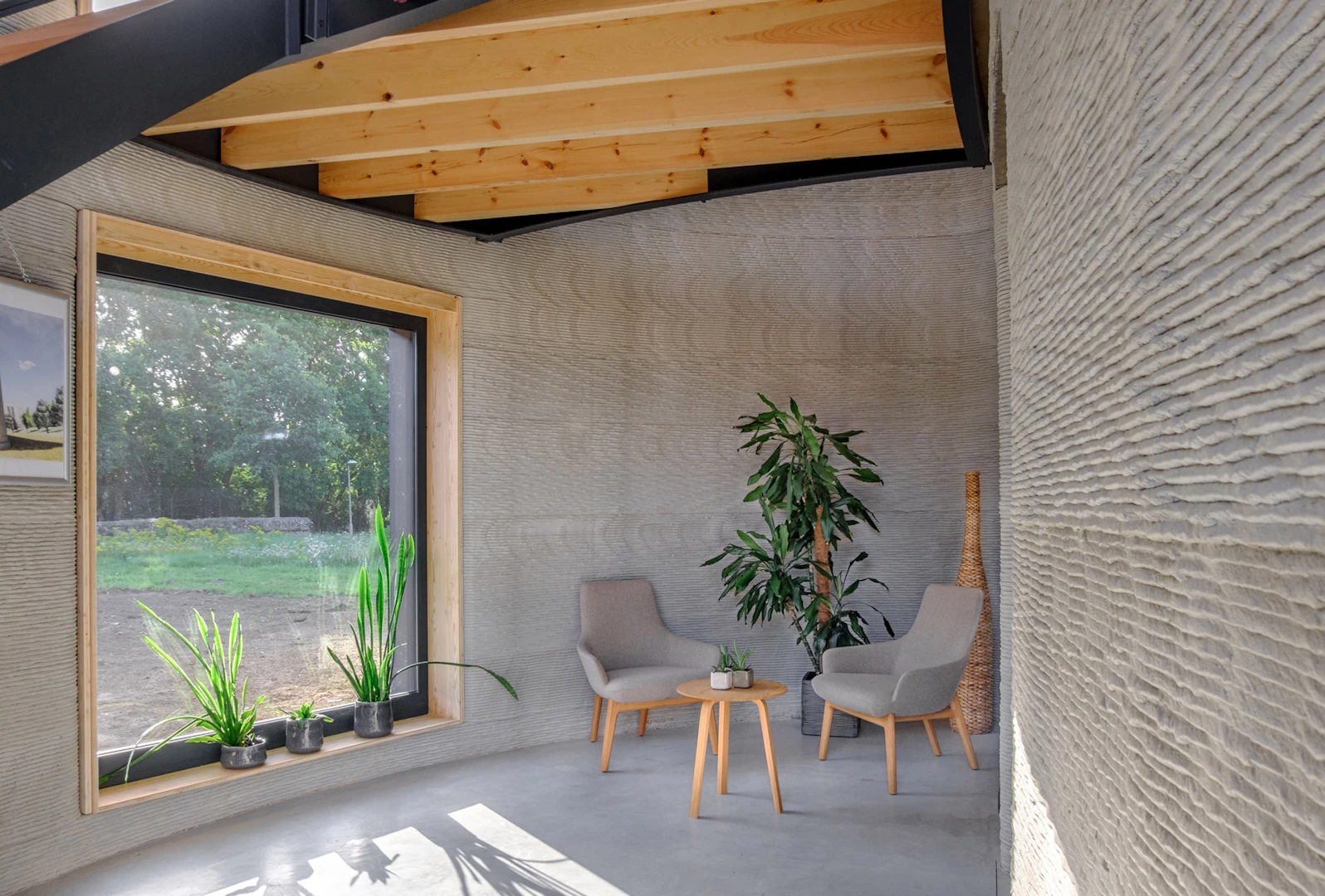 View of living area inside 3d printed concrete house with large window and wooden ceiling beams